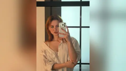 AlbertaCorrell takes a mirror selfie wearing a loose, white button-down shirt and a white lace bra.