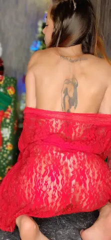 Woman with back tattoo wearing a red lace robe sitting in a cozy indoor setting.