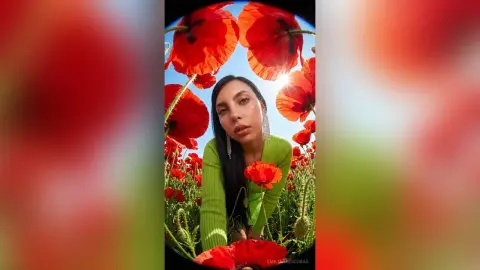 Young woman in a green ribbed top surrounded by vibrant red poppies in a sunny field.