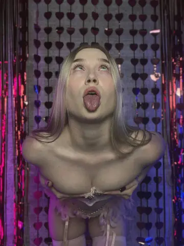 Blonde woman in white lace lingerie making a playful expression against a pink heart fringe backdrop.