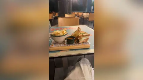 Delicious grilled cheese sandwich served with potato chips and dipping sauce on an outdoor cafe table at night.