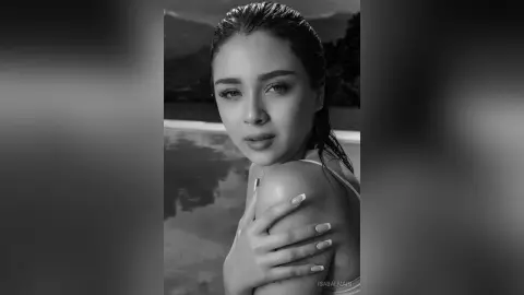 Black and white portrait of a beautiful woman with wet hair posing by a swimming pool at sunset.