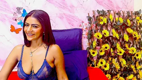 ChloeLanez — ChloeLanez smiles while wearing a blue lace camisole, sitting on a red sofa against a pink marble wall.