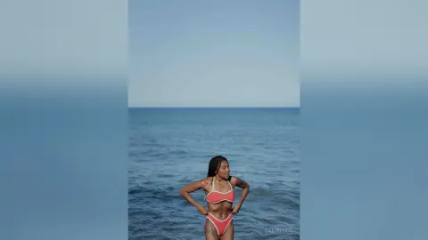Young woman in a coral bikini relaxing on a serene blue ocean beach under a clear sky.