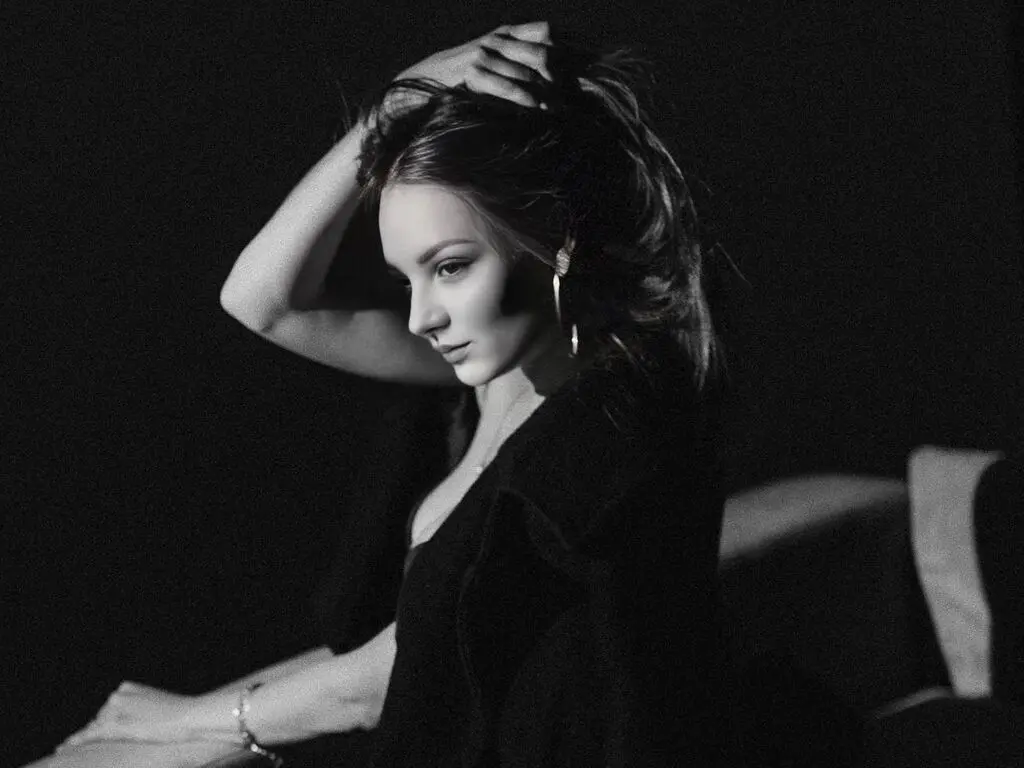 Moody black and white portrait of a woman in a black outfit posing with dramatic lighting in a dark setting.