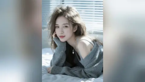 Young woman in a grey sweater relaxing on a bed in soft, bright sunlight for a cozy, dreamy mood.