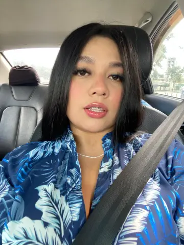 Young woman in a blue tropical print shirt sitting in a car seat with a relaxed mood.