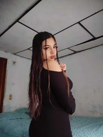 Young woman with long brown hair wearing a black off-the-shoulder dress in a minimalist room.