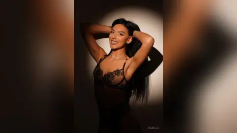 Iza — Smiling woman in black lace lingerie posing confidently against a minimalist studio background.