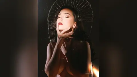 Elegant woman in glamorous gold headpiece posing with dramatic lighting in a moody, dark studio setting.