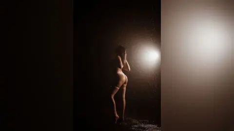Moody silhouette of a woman in white lingerie standing in a dark studio with dramatic backlight.