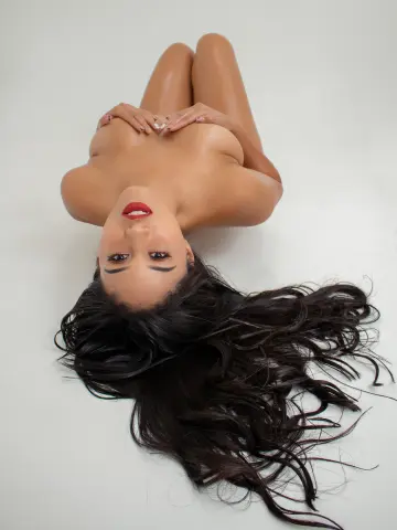 Beautiful woman with long dark hair lying on a white background in a serene, minimalist setting.