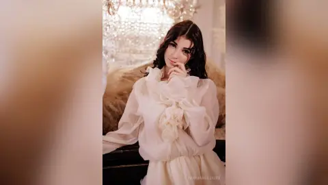 Elegant woman in a white ruffled blouse posing gracefully in a luxurious, bright interior setting.