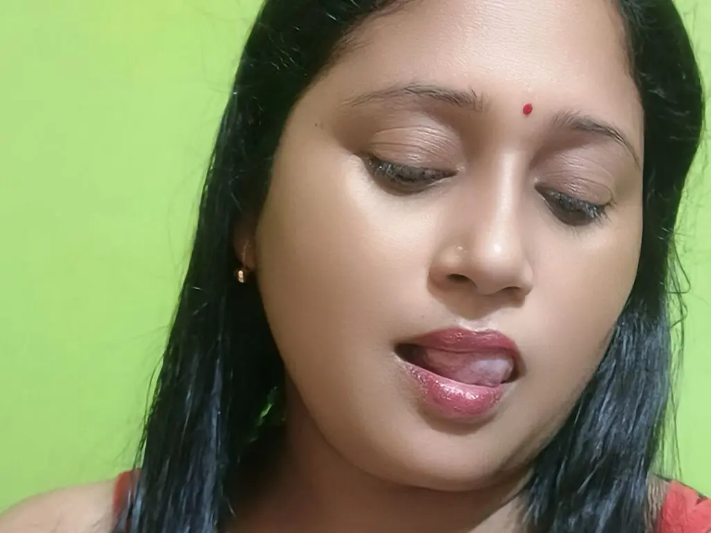 QueenPori looks down with her eyes closed and her tongue out against a bright green background.