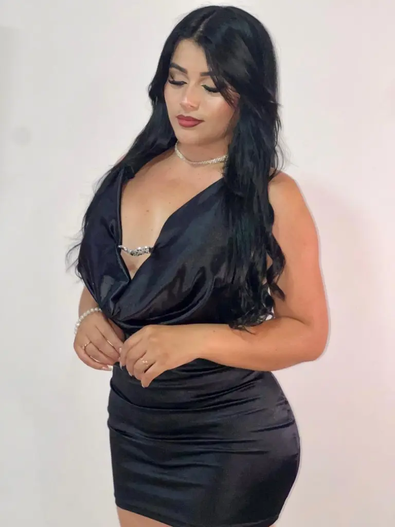 chloeblakee poses with her long black hair, wearing a low-cut black top that shows cleavage, while looking off to the side.