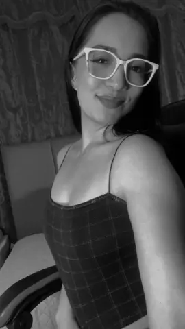 Smiling woman in a plaid spaghetti strap top posing in a moody indoor setting.