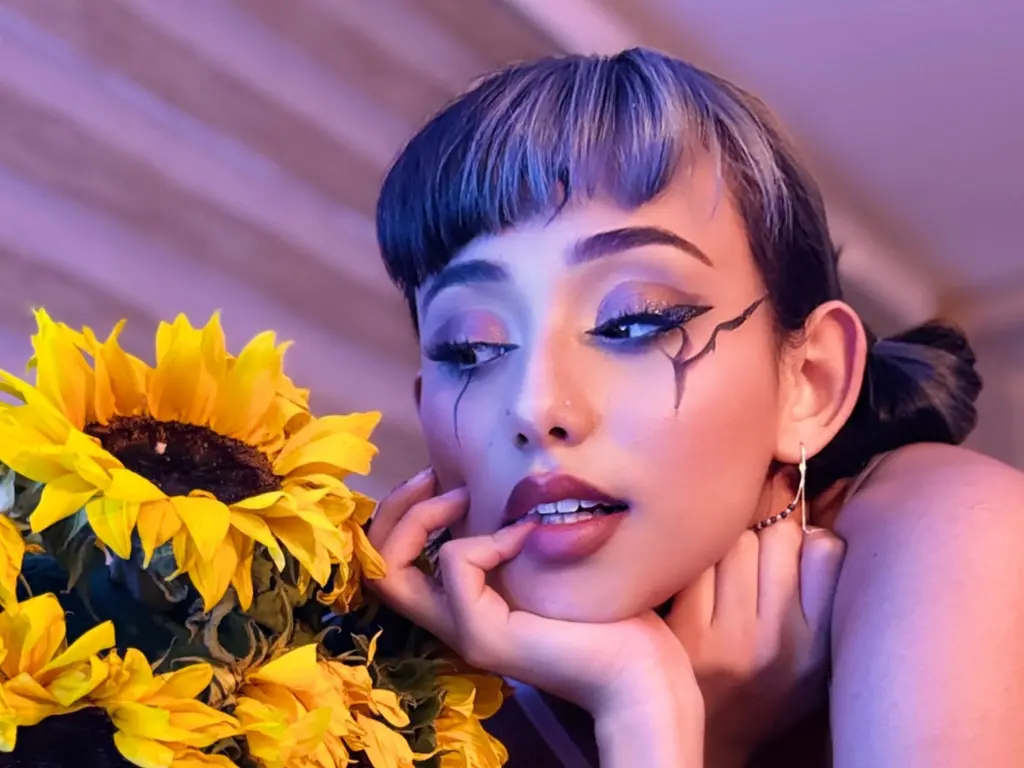 MartiinaAlvarez — Woman with artistic eyeliner posing with bright sunflowers in soft purple lighting.