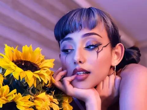 Woman with artistic eyeliner posing with bright sunflowers in soft purple lighting.