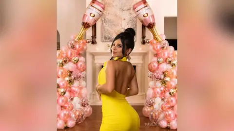 Glamorous woman in a yellow backless dress celebrating at a pink balloon party with champagne bottles.