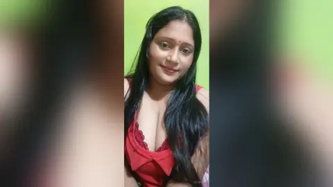 QueenPori poses in a red lace camisole with her long black hair falling over her shoulders against a lime green wall.