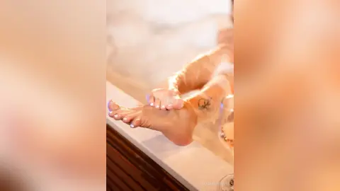 Close-up of a woman's feet with white pedicure relaxing in a warm, steamy spa bath setting.