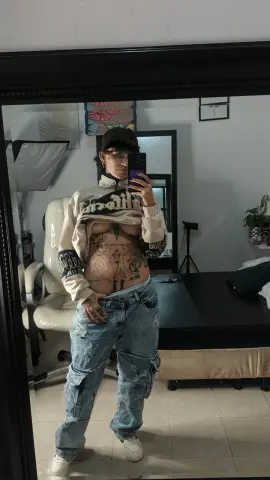 lucirosee poses in a mirror wearing a cropped white sweatshirt and baggy denim cargo pants, showing off her stomach tattoos.
