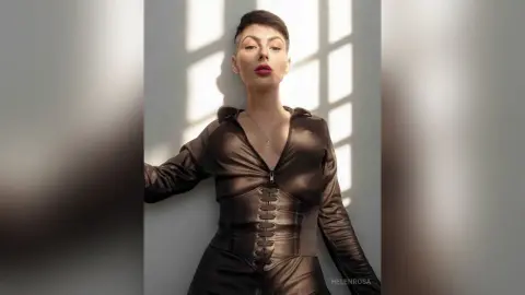 Elegant woman in a black leather corset outfit posing against a sunlit wall in a moody studio setting.