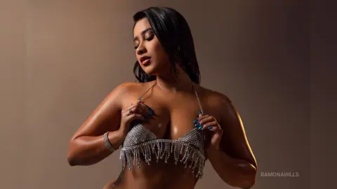 Glamorous woman in a sparkling silver sequin bikini top posing against a warm studio background.