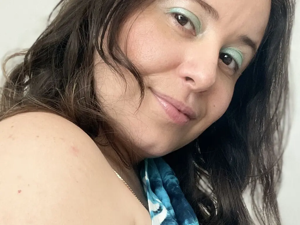 Smiling woman with long dark hair wearing a blue patterned top in a bright, natural setting.