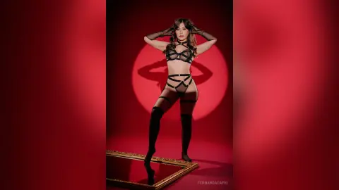Woman in black lace lingerie and thigh-high stockings posing against a red background with dramatic lighting.
