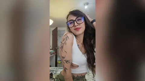 RossiNoleen wears a white cutout tank top and glasses while posing with her hand in her long dark hair.