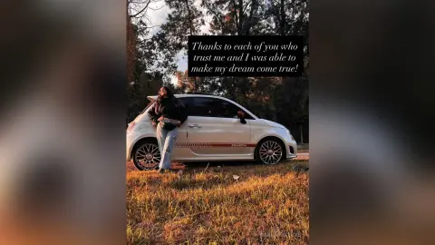 Woman in casual jeans and black top leaning on a white Abarth car in a golden hour forest setting.