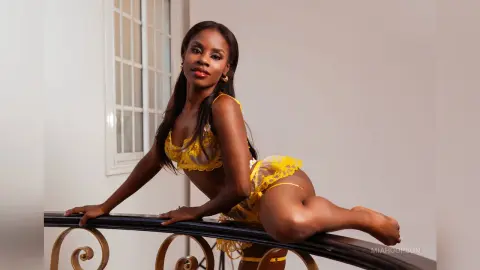 Confident Black woman in yellow lace lingerie posing by a window in a bright, minimalist room.