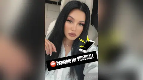 AnnaBanks poses with long black hair and heavy eye makeup, wearing a white button-down shirt while looking into the camera.