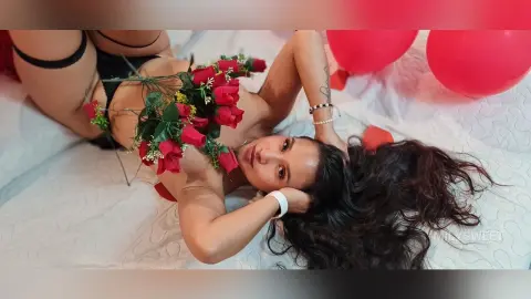 Young woman with long dark hair lying on white bedding covered in red roses for a romantic mood.