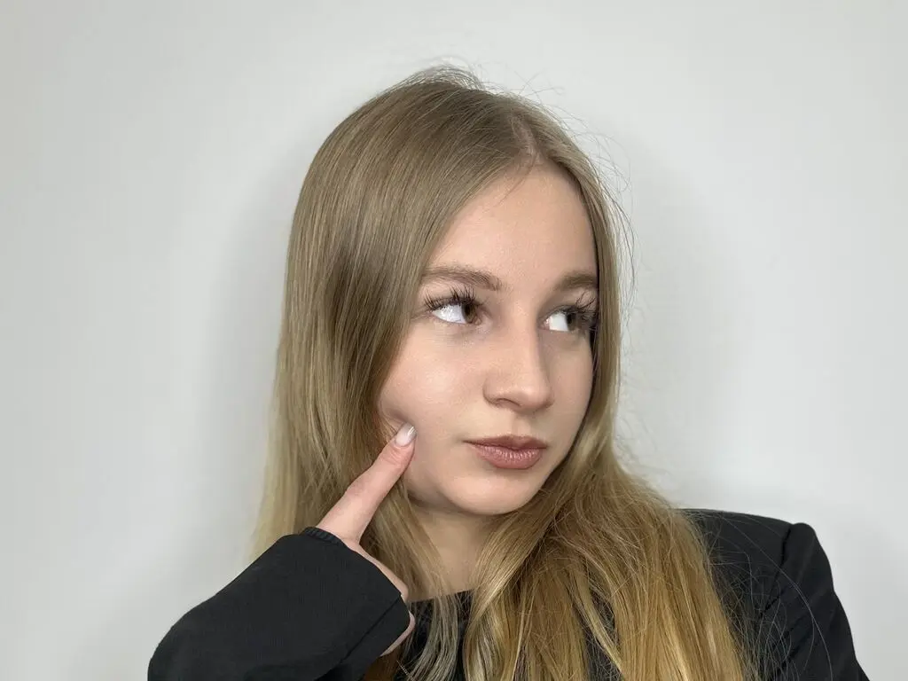 Blonde woman in a black outfit looking away with a thoughtful expression against a plain white background.