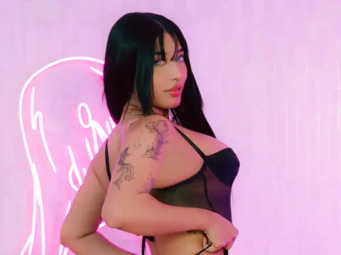 LilithOwens with long black hair and blue eyes poses in a black sheer bra against a pink neon background.