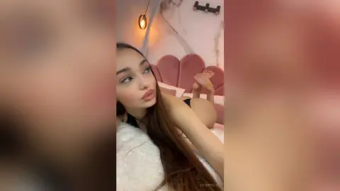 Young woman in black lingerie relaxing on a white bed in a cozy, dimly lit bedroom.