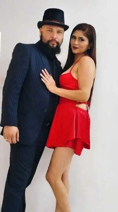 camila_dark — Elegant couple in formal attire posing together, featuring a man in a navy suit and a woman in a red cocktail dress.