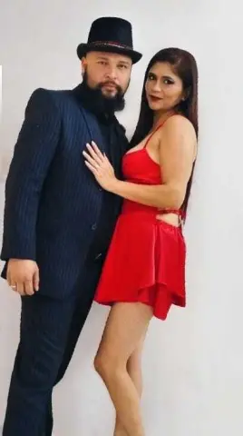 Elegant couple in formal attire posing together, featuring a man in a navy suit and a woman in a red cocktail dress.