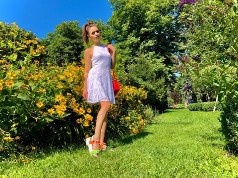 Young woman in a white summer dress and red bag standing in a sunny garden filled with yellow flowers.