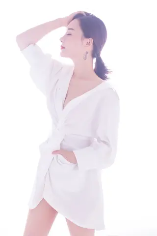 Serene woman in a white oversized shirt posing against a bright white background with a peaceful mood.