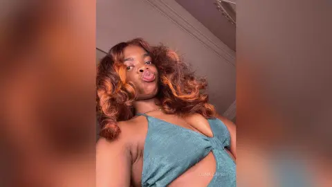 Playful woman in a teal halter top posing indoors with voluminous wavy brown hair.