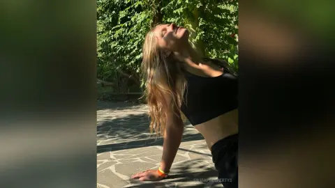 SilviaPrespertys poses outdoors in a black crop top and dark shorts, leaning back with her eyes closed in the sunlight.