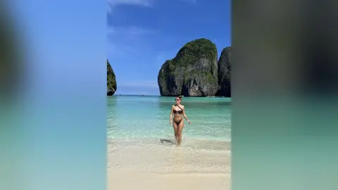 Woman in black bikini walking on a tropical beach with turquoise water and limestone cliffs in Thailand.