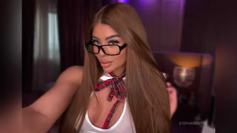 Beautiful woman with long brown hair wearing glasses and a white plaid tie in a moody, dimly lit room.