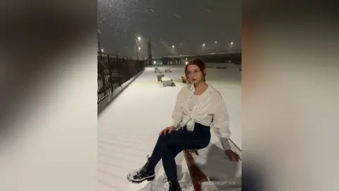 Young woman in white shirt and jeans sitting on a snowy bench during a peaceful winter night outdoors.