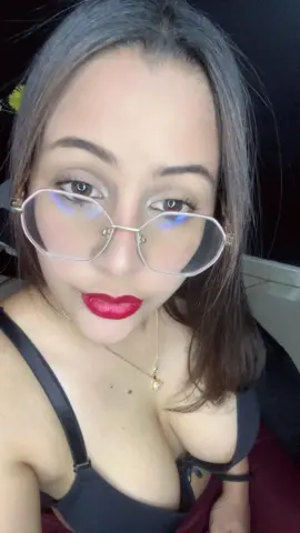 Young woman with glasses and red lipstick wearing a black tank top in a moody indoor setting.