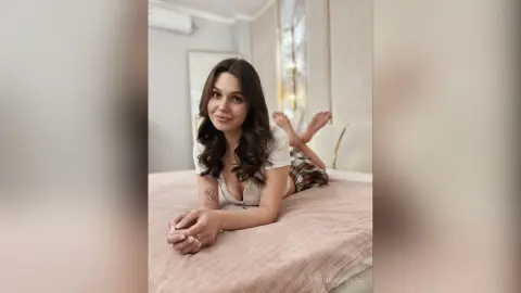 Young woman in white loungewear relaxing on a bed in a bright, cozy bedroom.