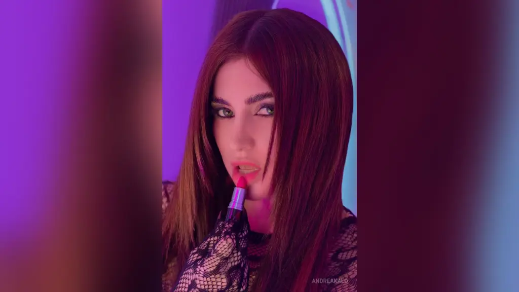 AndreaKalo poses in a sheer black lace bodysuit with long brown hair against a purple neon background.